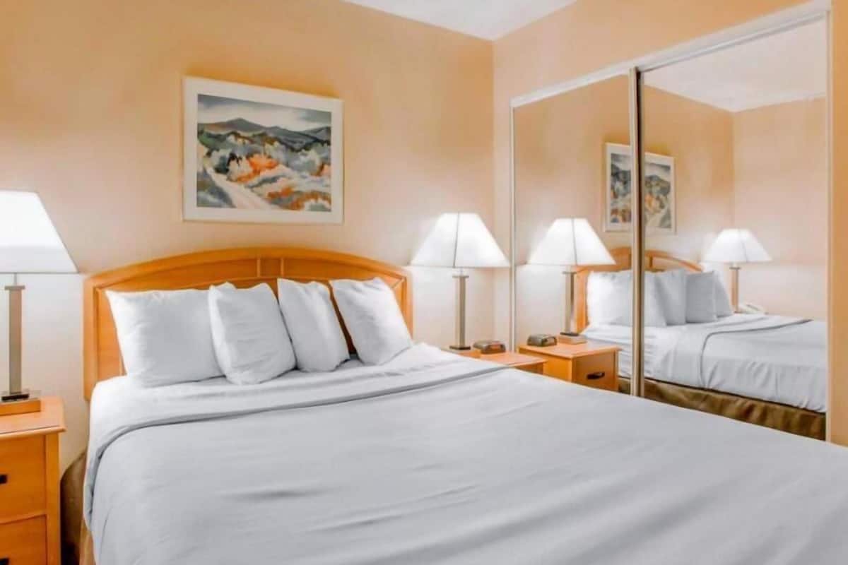 Ein Hotelzimmer mit einem großen Bett, zwei Nachttischen, einem Schminktisch, einem Spiegel und einem Bild an der Wand.