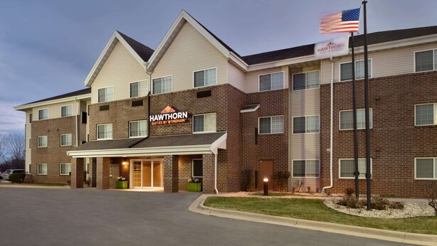 A multi-story hotel with a brick facade, a sign reading "Hawthorn Suites by Wyndham," and an American flag on a flagpole.