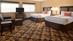 A hotel room with two beds, a TV, a desk, and a patterned carpet.