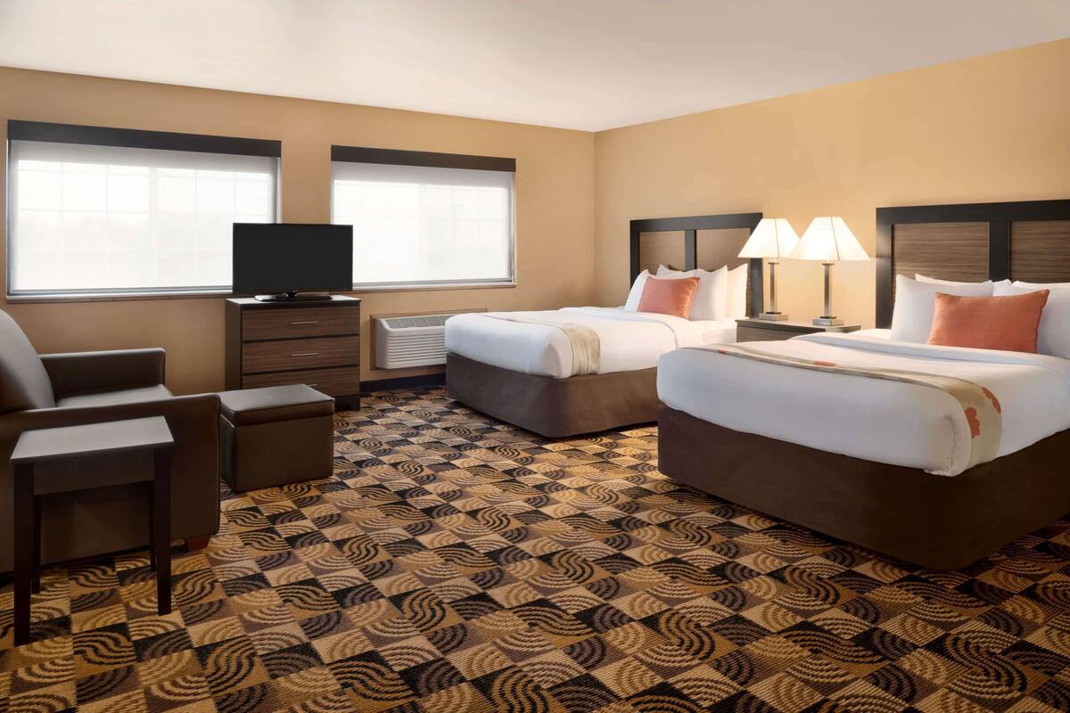 Ein Hotelzimmer mit zwei Betten, einem Fernseher, einem Schreibtisch und einem gemusterten Teppich.