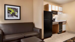 A compact living space with a sofa, a small ottoman, a kitchen area with a refrigerator, microwave, and cabinets.
