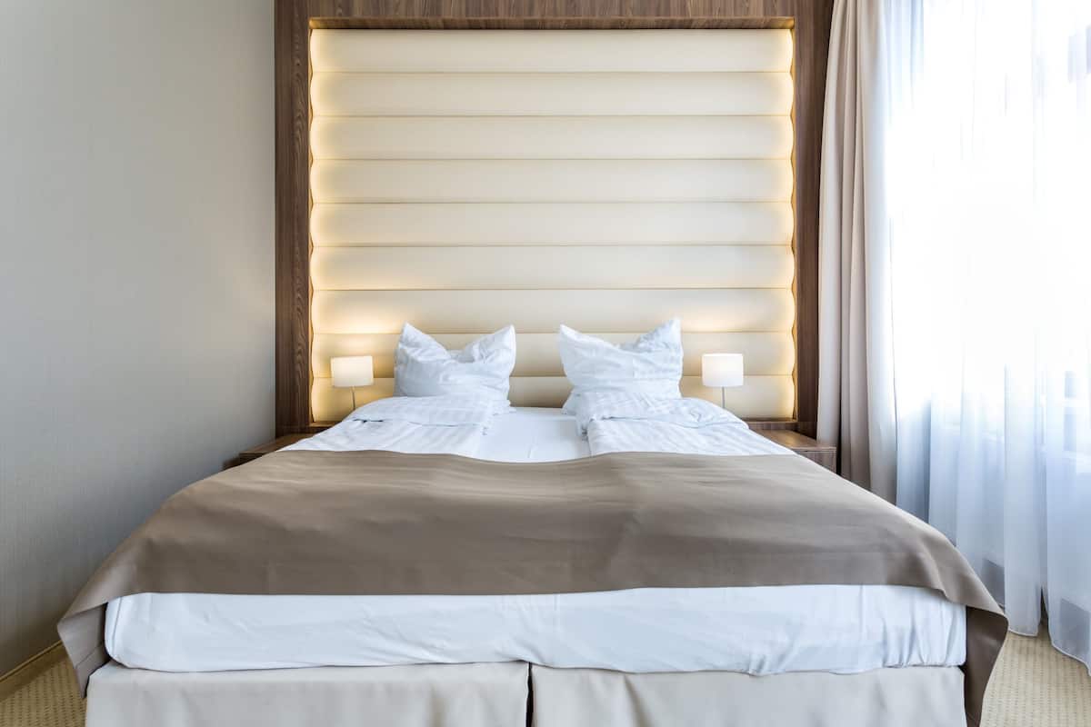 A neatly made bed with a beige and white color scheme, a wooden headboard, and bedside lamps.