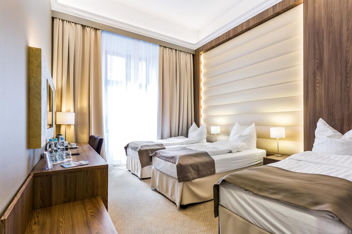 A hotel room with two beds, a desk with a chair, and a large window with curtains.