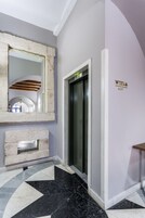 A modern elevator with a glass door, a stone-framed mirror, and a "Winda Lift" sign on the wall.
