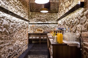 A stone-walled room with a breakfast bar, shelves with plates, and a variety of food and drink items.
