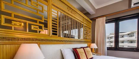 A hotel room with a large bed, two bedside lamps, a decorative headboard, and a view of buildings through the window.