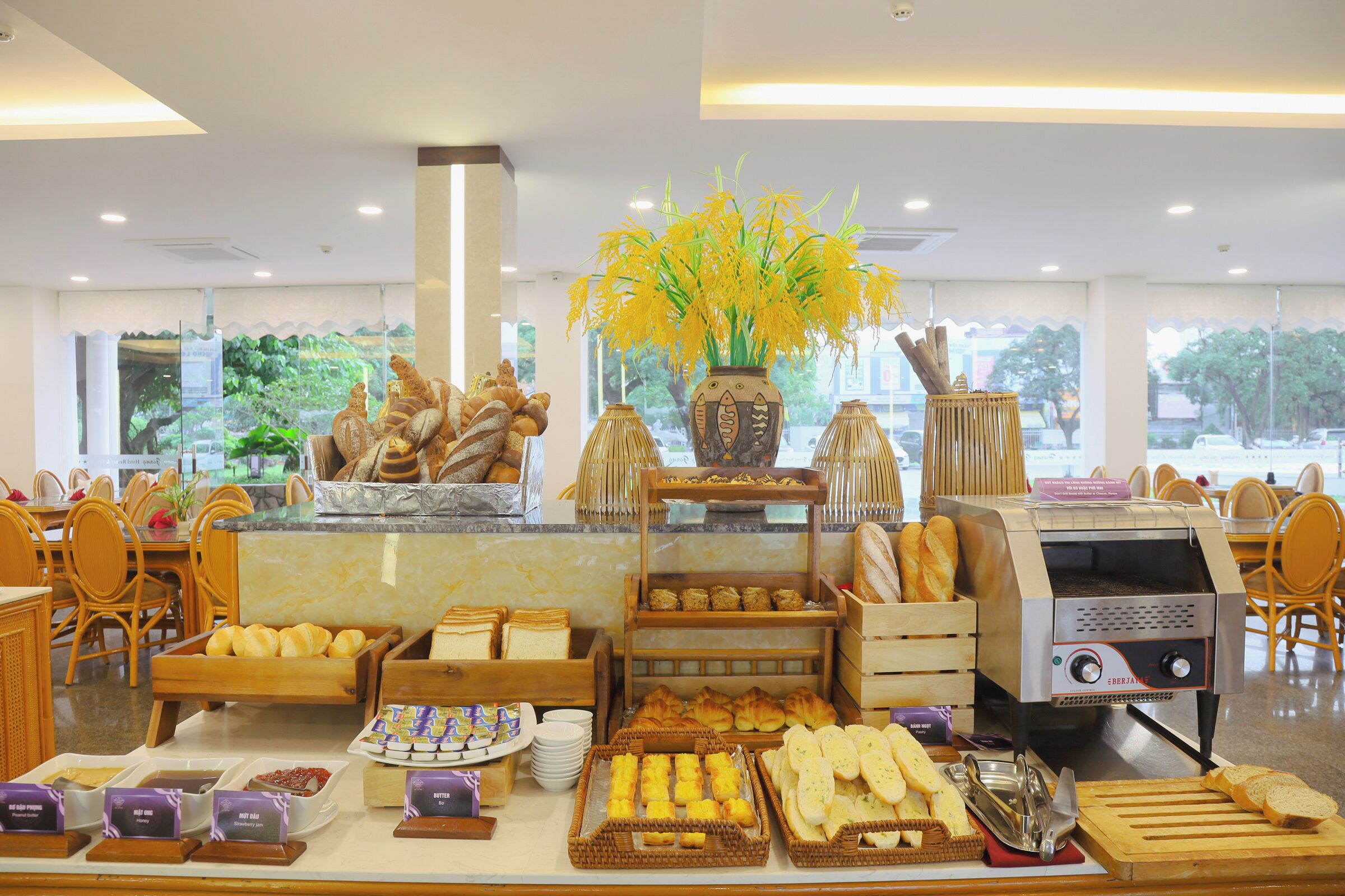 A buffet area with various food items, a coffee machine, and a vase with yellow flowers.