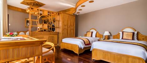 A room with two beds, a wooden desk, wicker chairs, and a decorative ceiling.