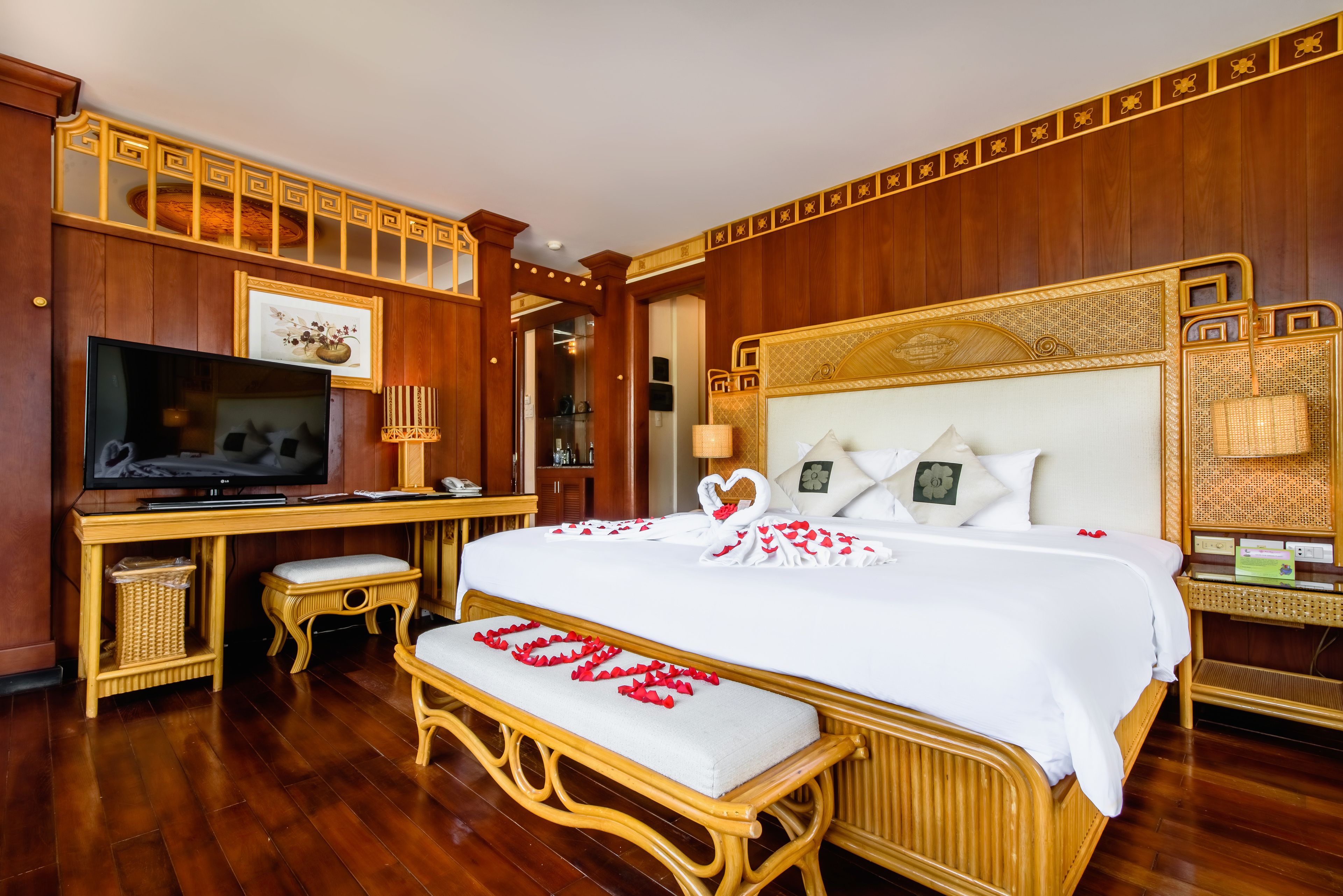 A hotel room with a large bed, a television, a desk, and wicker furniture.