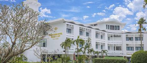 A modern hotel with a white facade, multiple balconies, and a clear sky.