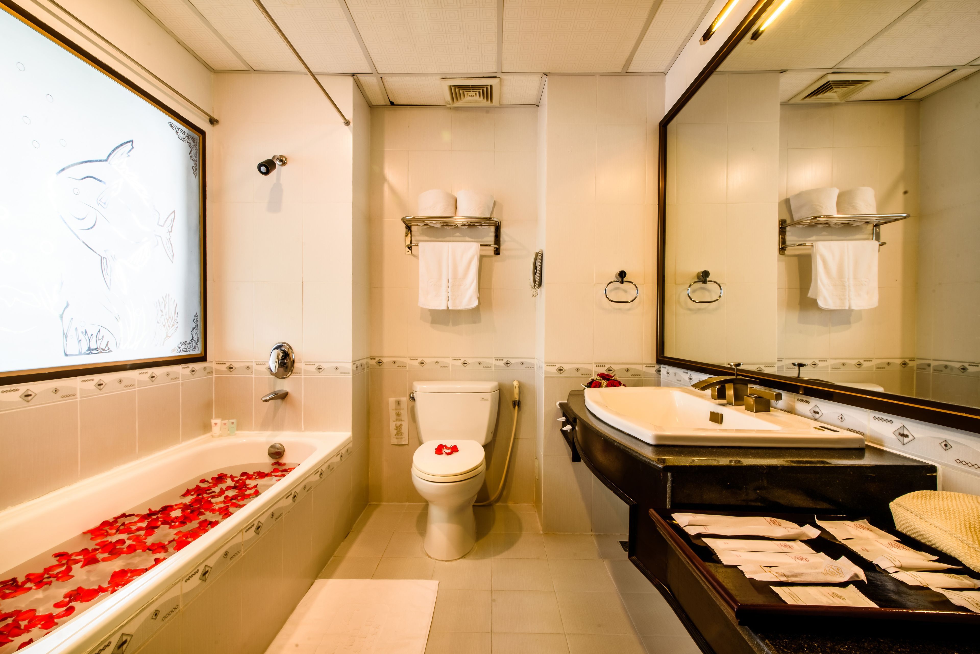 A bathroom with a bathtub filled with rose petals, a toilet, a sink, and a large mirror.