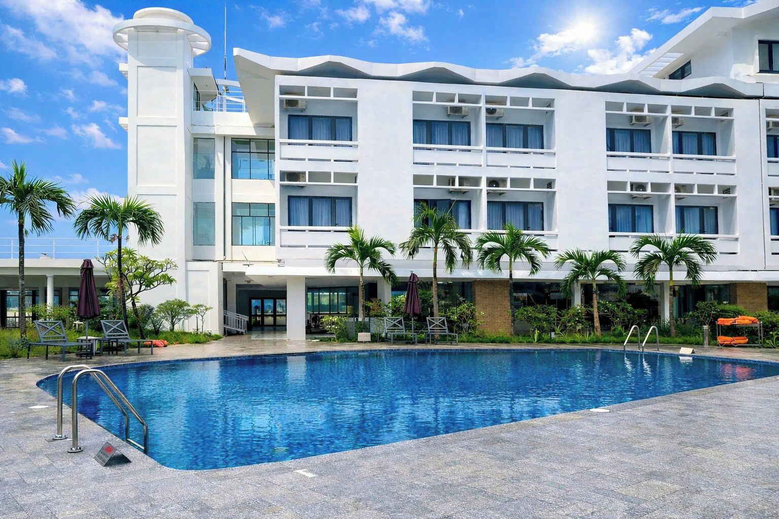A modern hotel with a large pool, multiple balconies, and palm trees.