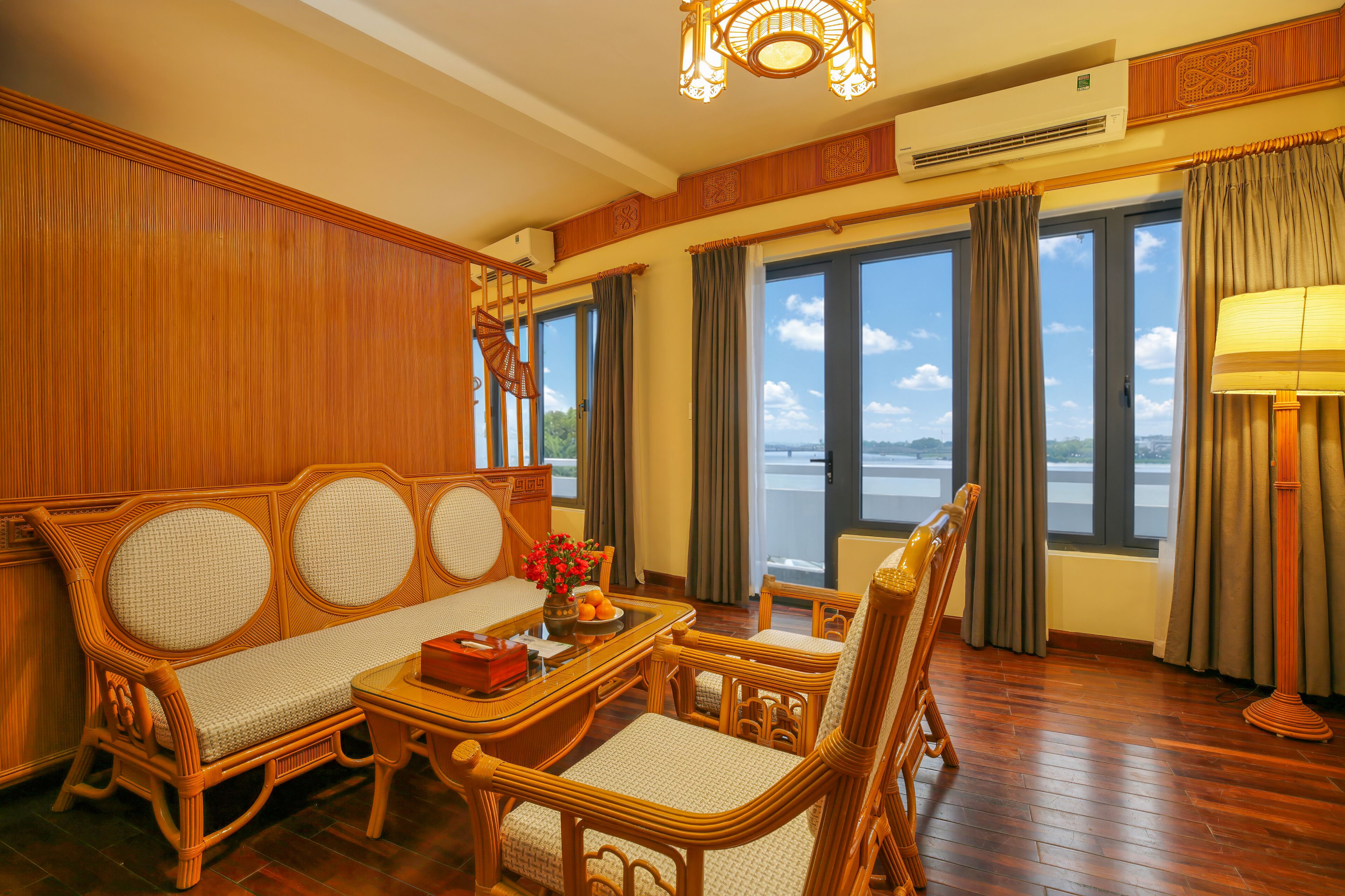 A traditional room with a sofa, chairs, a table with a vase, and a view of a body of water through large windows.