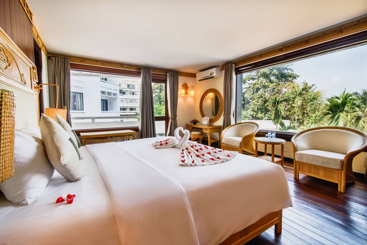 Hotelkamer met een groot bed, een zithoek met een fauteuil en een tafeltje, een spiegel en uitzicht.
