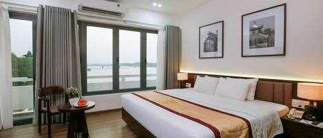 A hotel room with a large bed, a bedside table, a chair, a window with curtains, and two framed pictures on the wall.