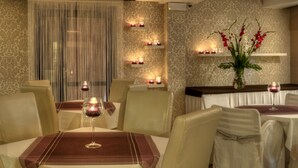 A restaurant with a warm ambiance, featuring candle-lit tables, elegant chairs, and a decorative vase with flowers. - Petrus Hotel (Kraków)