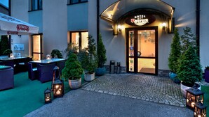 A hotel entrance with a sign reading "Hotel Peterus," outdoor seating with tables and chairs, and potted plants. - Petrus Hotel (Kraków)