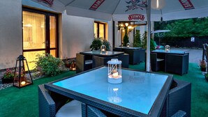 An outdoor patio area with wicker furniture, glass-top tables, and potted plants. - Petrus Hotel (Kraków)