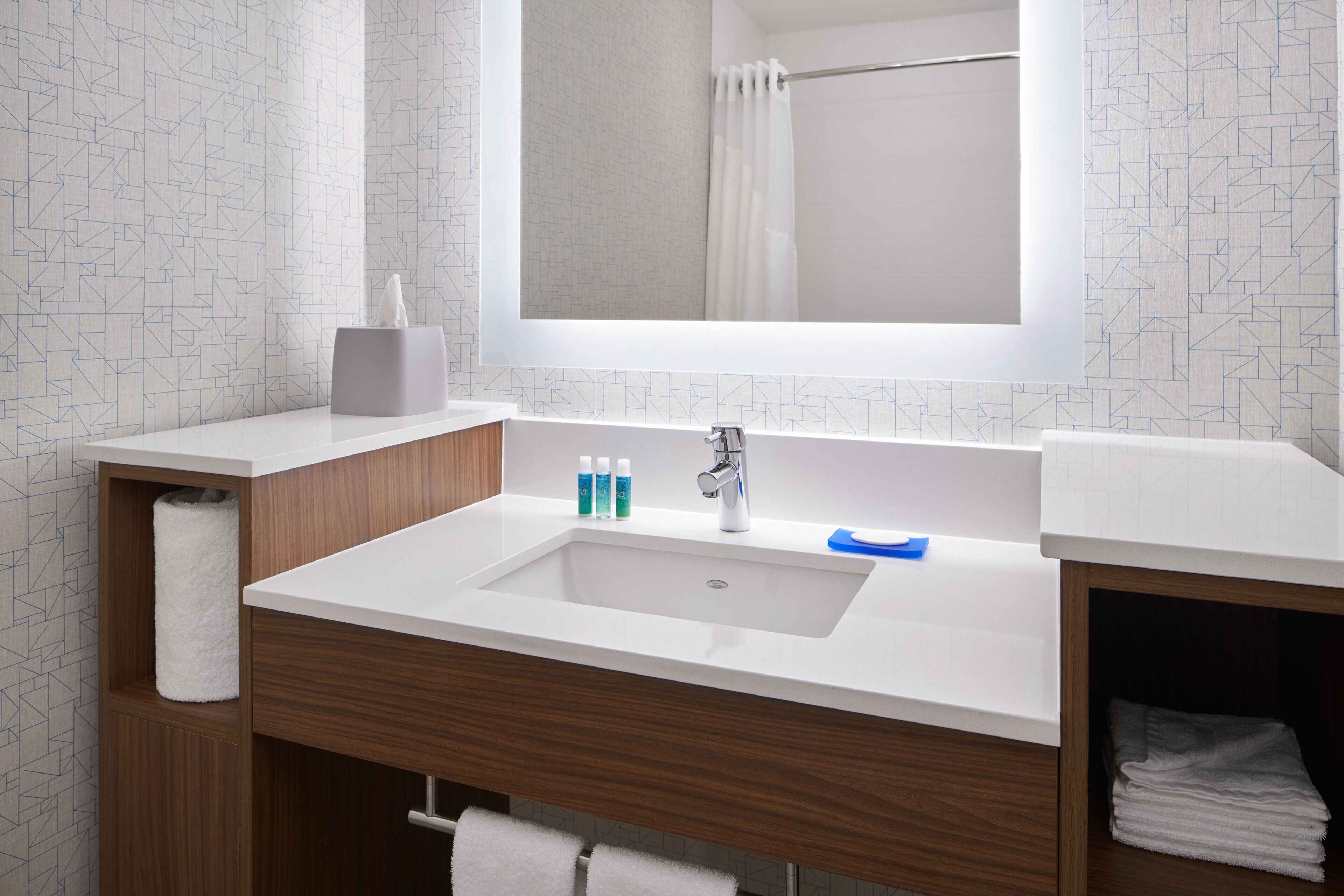A modern bathroom with a white sink, wooden vanity, and a mirror above the sink.