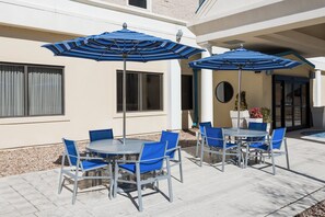 An outdoor patio area with tables and chairs, blue umbrellas, and a building facade. - Holiday Inn Express Richmond Downtown by IHG (Richmond)