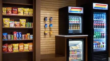 A snack display with various chips and snacks, a small refrigerator with beverages, and a larger refrigerator with sodas.