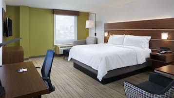 Habitación de hotel con cama, escritorio, silla, televisión y ventana con vista a la ciudad.