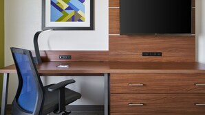 A modern hotel room with a wooden desk, a black office chair, a flat-screen TV mounted on a wooden cabinet, and a framed abstract art piece on the wall. - Holiday Inn Express Richmond Downtown by IHG (Richmond)