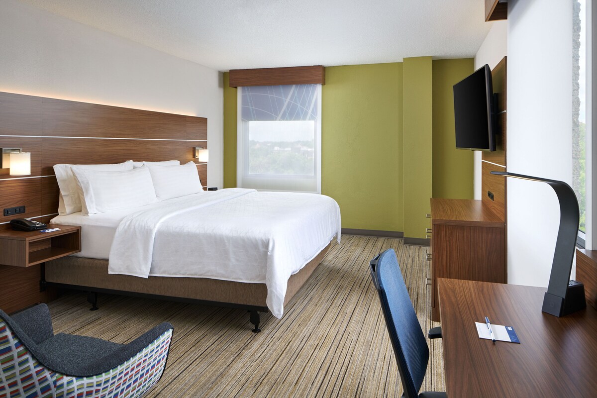 A hotel room with a bed, bedside table, chair, desk, TV, and window.