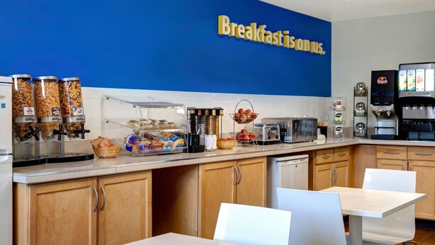 Una estación de desayuno con pared azul, diferentes dispensadores de comida, una máquina de café y un tostador.