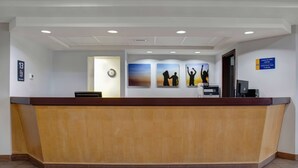Mostrador de recepción en Days Inn by Wyndham, con un reloj, obras de arte y un cartel que indica la hora de registro.