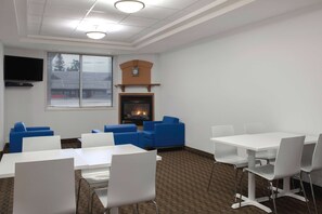 Uma sala de conferências com mesas brancas e cadeiras azuis, lareira e uma televisão na parede.