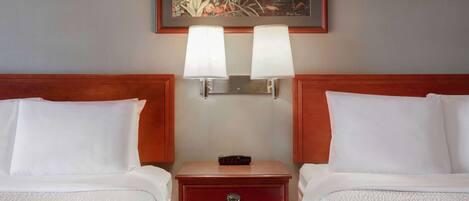 A hotel room with two beds, a nightstand with a clock, and a painting above the nightstand.