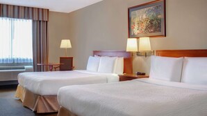 Habitación de hotel con dos camas, un escritorio, una silla, una lámpara y un cuadro en la pared.