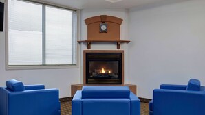 Una habitación con chimenea, dos sillones azules y una ventana con persianas.