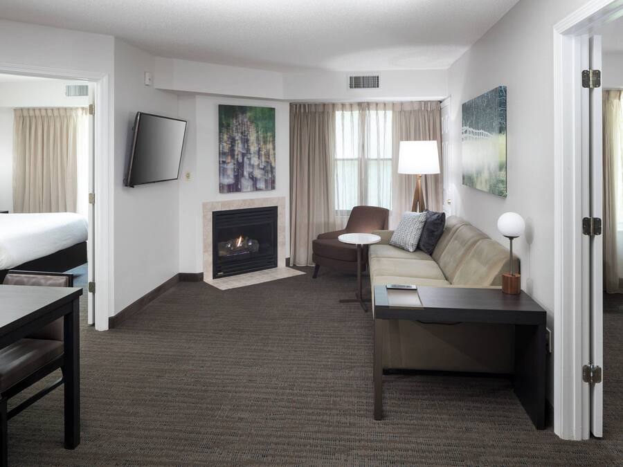 A hotel room with a bed, a sofa, a desk, a fireplace, and a TV.