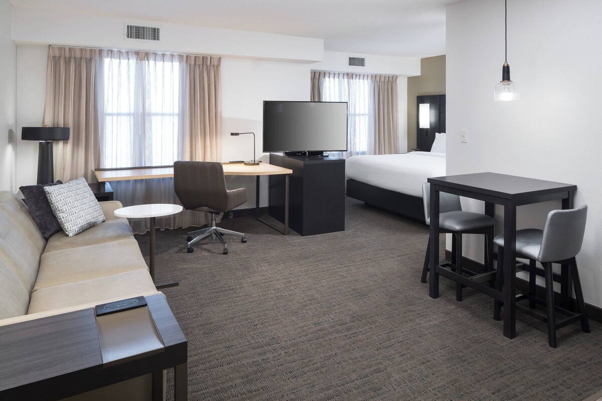 Habitación de hotel con cama, escritorio con televisor, sofá y dos sillones.