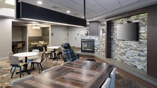 A modern meeting room with a large wooden table, comfortable seating, a fireplace, and a flat-screen TV mounted on a textured wall. - Residence Inn by Marriott Boston Westford (Westford)