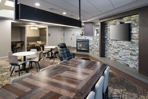 A modern meeting room with a large wooden table, comfortable seating, a fireplace, and a flat-screen TV mounted on a textured wall. - Residence Inn by Marriott Boston Westford (Westford)