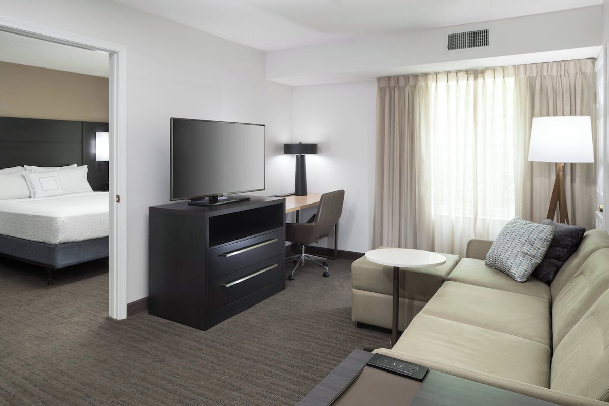 Habitación de hotel con cama, televisión, escritorio, silla, sofá y lámpara.