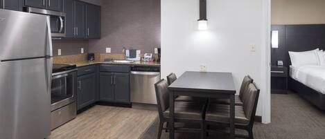 A modern kitchen with stainless steel appliances, a dining area with a table and chairs, and a separate bedroom with a bed and nightstand.