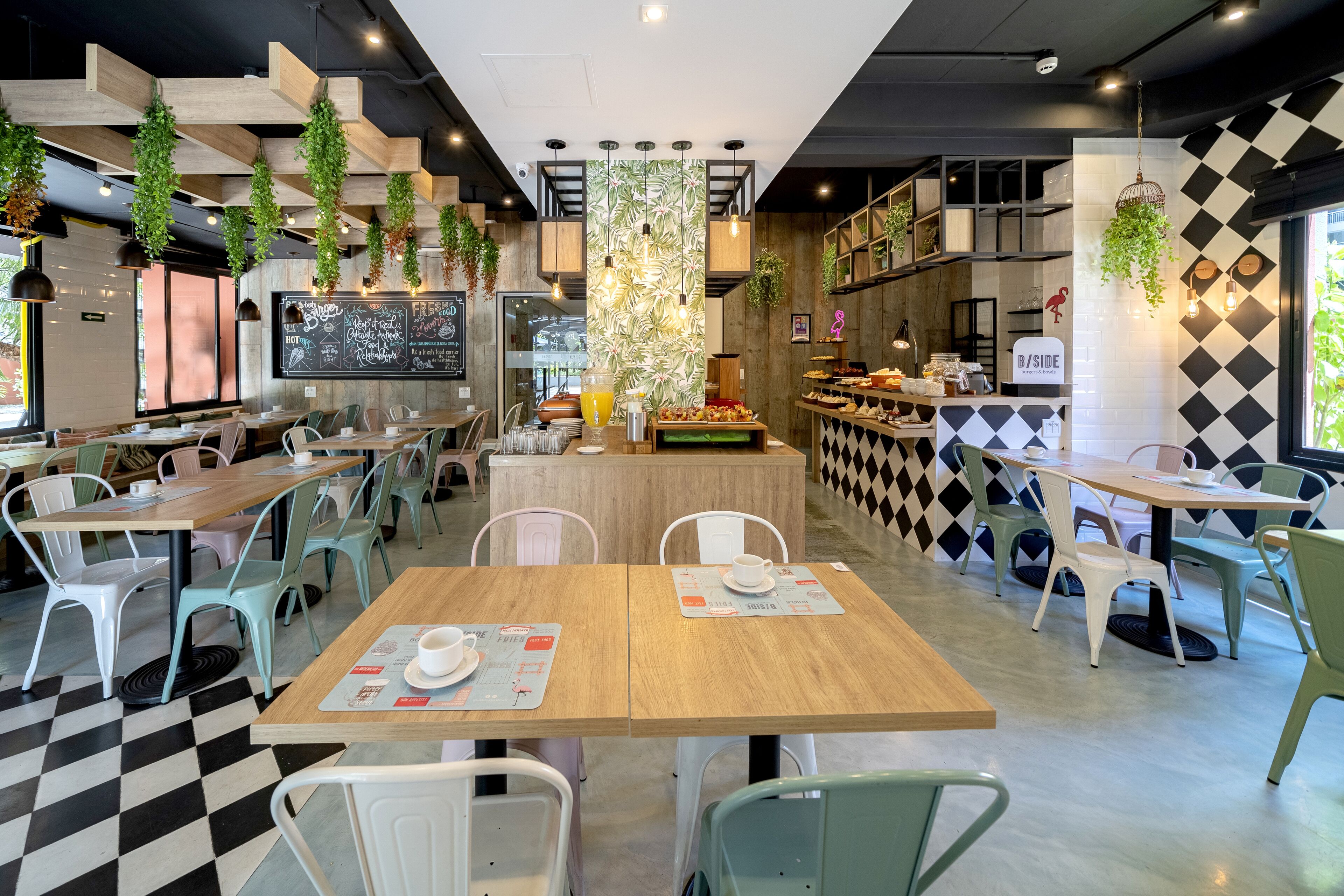 Ein Restaurant mit Holztischen und -stühlen, einer Kreidetafel als Speisekarte und hängenden Pflanzen.