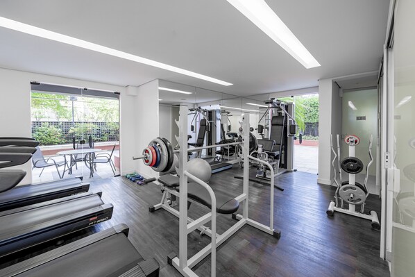 Une salle de sport moderne équipée de tapis de course, d’appareils de musculation et d’un mur entièrement recouvert de miroirs.