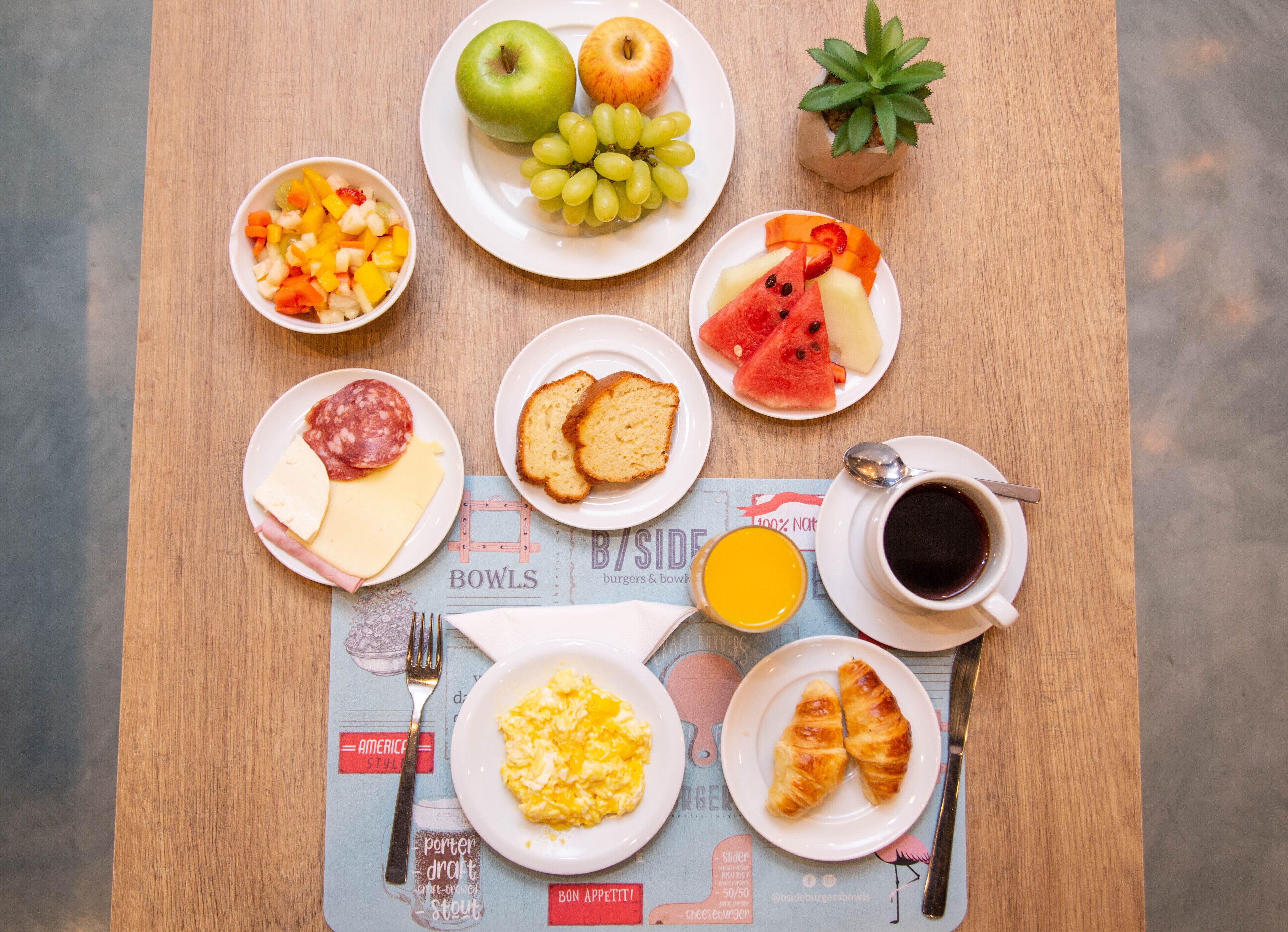 A breakfast table with various food items, including fruits, bread, cheese, and eggs.