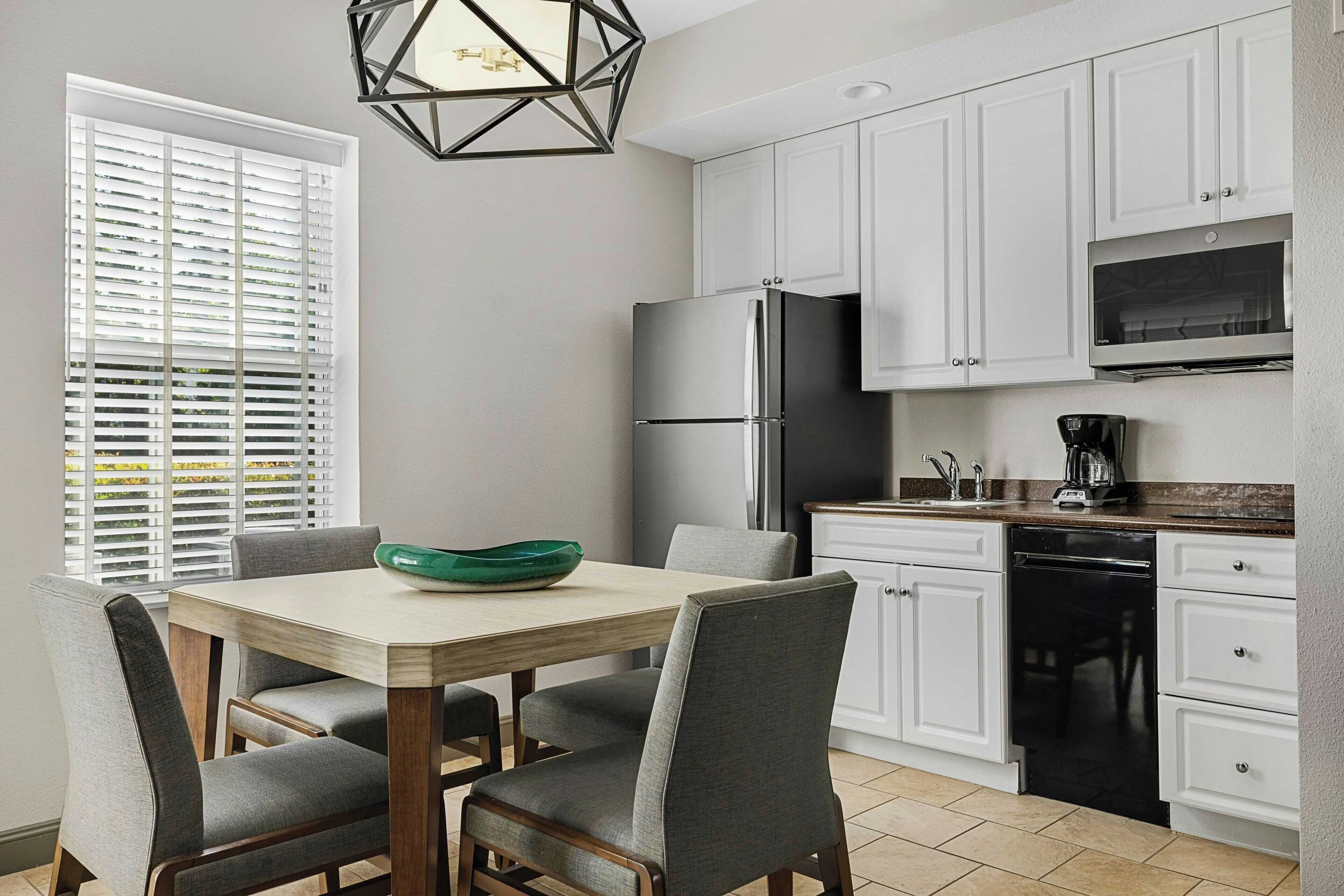 A kitchen with white cabinets, a stainless steel refrigerator, a dishwasher, and a dining table with chairs.