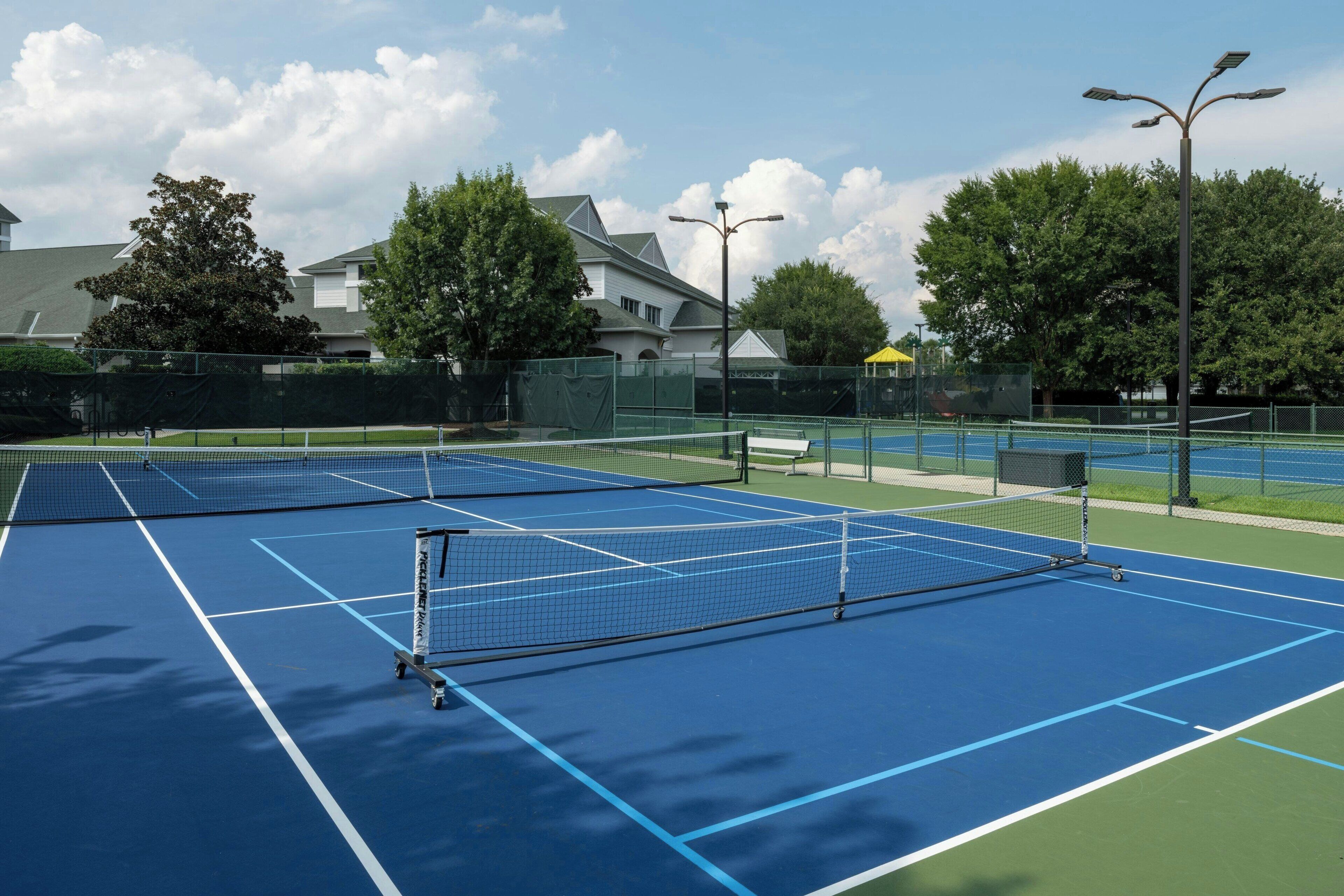 Un court de tennis avec un filet, entouré d’une clôture verte et d’arbres.
