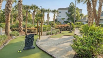 Un campo de mini golf con una estatua, palmeras y un edificio al fondo.