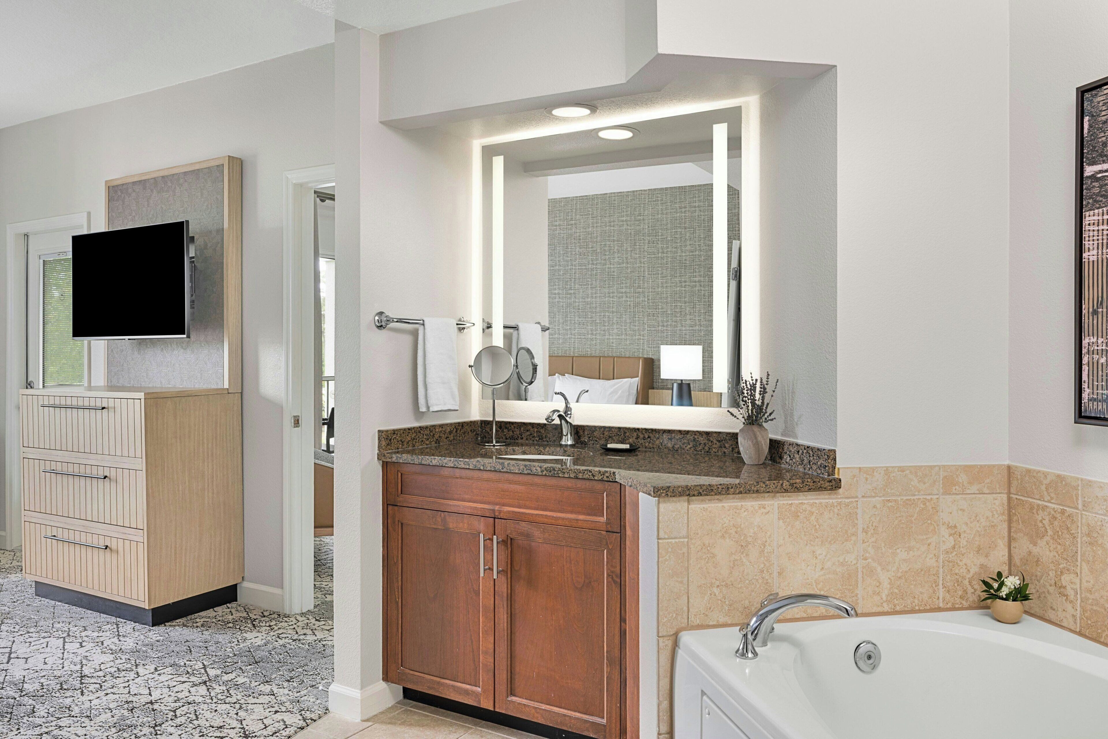 A modern bathroom with a large mirror, a sink, and a bathtub.