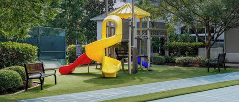 A playground with a slide, a climbing structure, and a shuffleboard court.