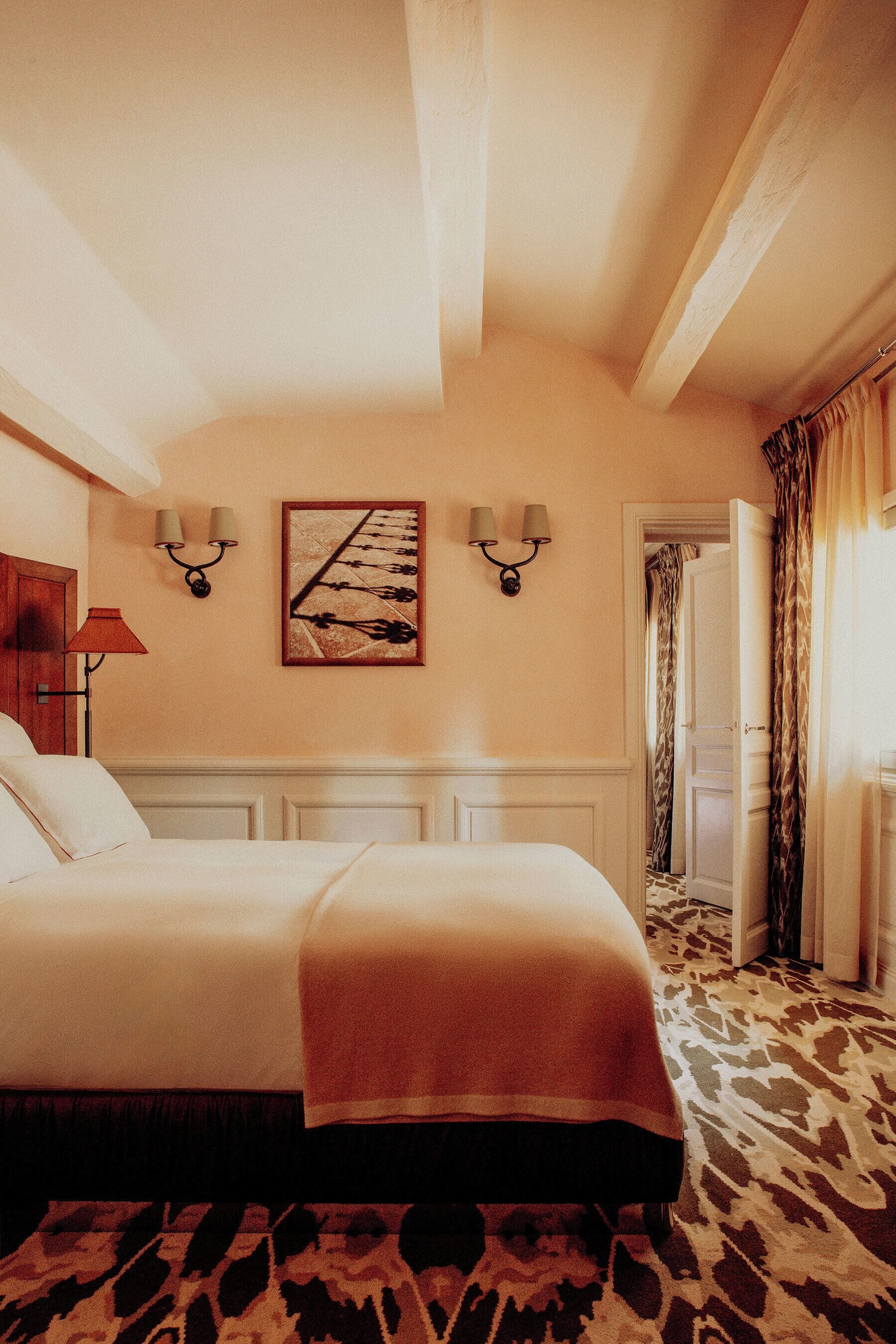 Une chambre d’hôtel avec un grand lit, une tête de lit ornée d’un panneau décoratif, un luminaire fixé au mur et un tableau encadré.