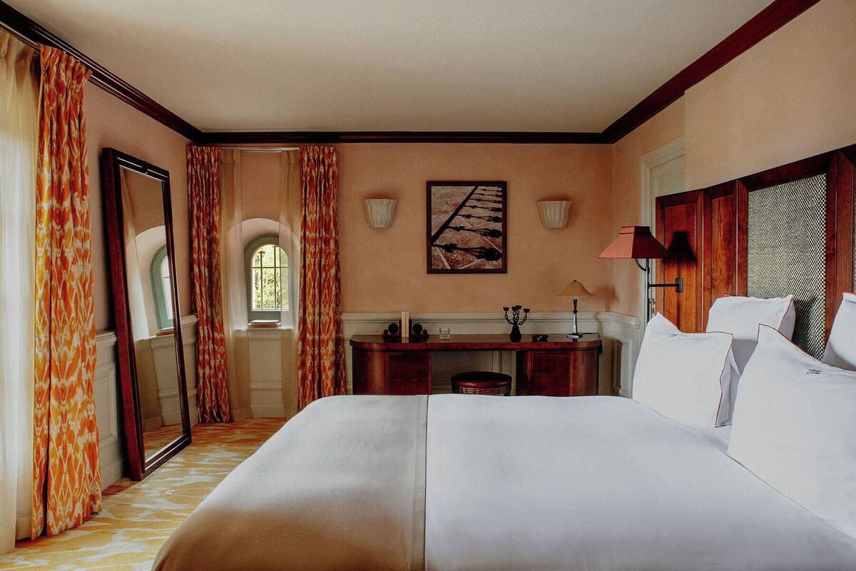 A hotel room with a large bed, a desk, a mirror, and a window with curtains.